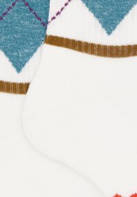 Calzini bianchi con motivi a rombi blu e strisce marroni vicino alla parte superiore, mostrando una texture lavorata a maglia e parte dell'area del piede.