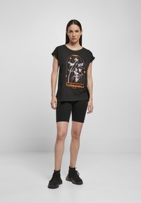Black cotton t-shirt with short sleeves, featuring a graphic design in orange and purple. Worn with black shorts and black sneakers.