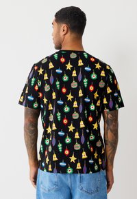 Sort kortærmet t-shirt med et flerfarvet mønster af ornater og stjerner, med en afslappet pasform og struktureret stof.