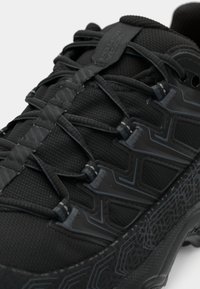 Zapatilla deportiva negra con parte superior texturizada, cordones planos y suela con patrón. Acentos lisos y ojales reforzados aumentan la durabilidad.