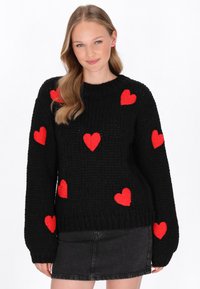 Schwarzer Strickpullover mit strukturierten roten Herzpatches, die über den Stoff verteilt sind. Rundhalsausschnitt und gerippte Bündchen.