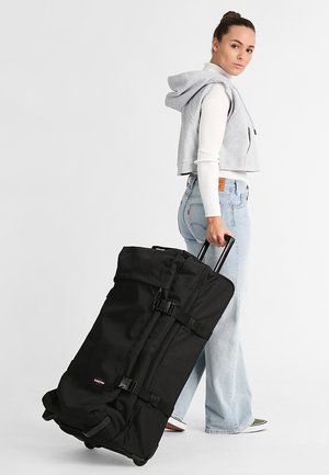 Sac de voyage à roulettes noir, fabriqué en tissu durable, doté de boucles ajustables, de deux poignées et d'une poignée télescopique pour un transport facile.