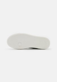 Suola di scarpa in gomma bianca con texture rigata orizzontale e verticale. Presenta un logo rotondo e una minimale brandizzazione su un lato.