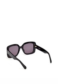 Store, sorte firkantede solbriller med mørke tonede linser og tykke, blanke stel, der ligger på en hvid overflade.