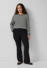 Schwarz-weißer gestreifter Langarmoberteil mit gerippter Textur, kombiniert mit schwarzen Schlaghosen und schwarzen flachen Schuhen mit Strassakzenten.