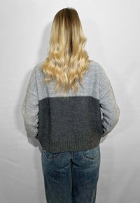 Maglione grigio e grigio chiaro a maglia con design cropped. Tessuto testurizzato con orlo a coste, indossato sopra jeans in denim a vita alta.