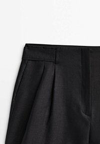 Pantalons noirs avec une finition lisse et texturée. Comprend une taille large, des plis et des poches latérales. Coupe ajustée et design à jambes droites.
