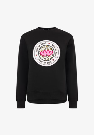 Schwarzer Pullover mit einem kreisförmigen Leopardenmuster, zwei rosa Herzen und dem weißen Schriftzug „wild at heart“. Lange Ärmel.
