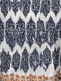 Hvitt stoff med gjentatte intrikate svarte blomster- og paisleymønstre, avgrenset nederst av en rad brune bladmønstre.