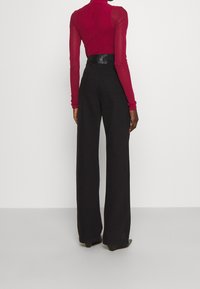 Maglietta rossa a maniche lunghe con maniche trasparenti abbinata a pantaloni neri a vita alta e gamba larga, con una vita liscia e una texture elegante.