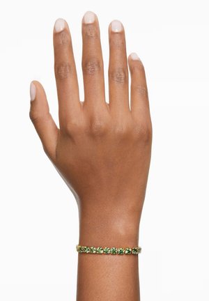 Gold bracelet with green gemstones arranged in a row. Worn on a hand with a smooth texture and neutral nail color.