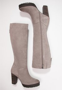 Höga taupe suede stövlar med kraftiga staplade klackar, rund tå och sidodragkedjor, visade mot en vit bakgrund.