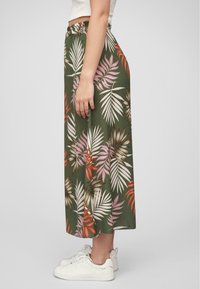 Lunga gonna verde con un motivo di foglie tropicali in tonalità di rosa e arancione, con una vita elastica e una vestibilità dritta, abbinata a sneaker bianche.