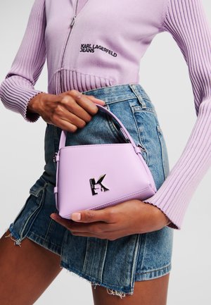 Lilac handbag with a structured design, featuring a silver monogram logo on the front. Paired with a purple ribbed sweater and denim skirt.