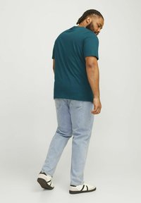 Teal kortærmet t-shirt, rund hals, passer løst, parret med lyseblå straight-leg jeans og casual hvide sneakers med sorte detaljer.