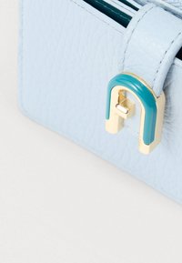 Γωνία τσάντας από γαλάζιο δερματίνη με υφή, με χρυσό και τιρκουάζ U-σχήμα κούμπωμα σε λευκό φόντο.