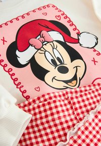 Bluza Minnie Mouse z różową grafiką, czerwoną czapką świąteczną i białym kołnierzykiem; posiada spódnicę w czerwoną i białą kratę z falbaną.