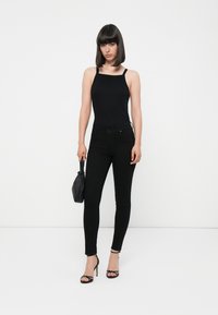 Juodas bodysuit'as su plonomis petnešomis, derinamas su juodomis aukštu liemeniu liesomis džinsinėmis kelnėmis ir juodais aukštakulniais sandalais. Aksesuarai apima mažą juodą rankinę.