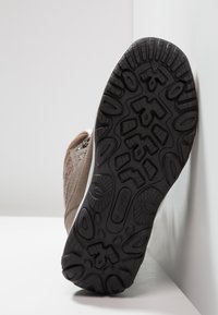 Bruine wandelschoen met een leren bovenwerk met textuur, witte tussenzool en een zwarte rubbere buitenzool met diepe noppen voor grip.
