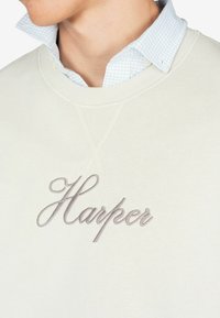 Felpa crema con finitura testurizzata, caratterizzata da un logo ricamato "Harper" grigio sul petto e con un collo a camicia a quadri blu chiaro sovrapposto.
