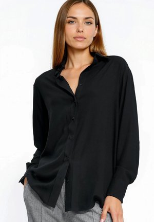 Czarna koszula na guziki z kołnierzykiem, długimi rękawami i luźnym krojem. Gładka tekstura i subtelny połysk. W zestawie z wzorzystymi spodniami.