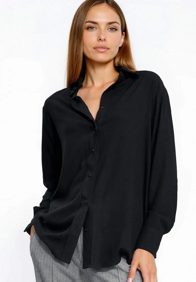 Czarna koszula na guziki z kołnierzykiem, długimi rękawami i luźnym krojem. Gładka tekstura i subtelny połysk. W zestawie z wzorzystymi spodniami.