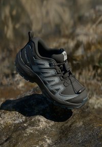Schwarz-grauer Wanderschuh mit einer strukturierten Oberseite, robuster Sohle und einem sicheren Schnürsystem. Mit einer Schlaufe zum einfachen Anziehen.