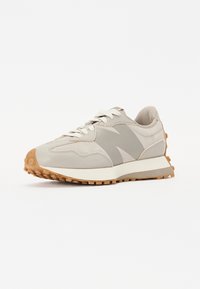Zapatilla con una parte superior de un beige claro, acentos grises y una suela de goma texturizada. Presenta una suela acolchada y un sistema de lazado tradicional.