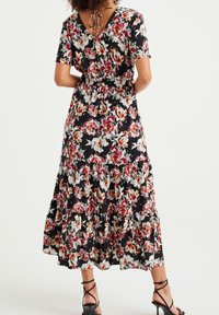 Blommig maxiklänning med svart bakgrund, prydd med röda och vita blommor, korta ärmar, v-ringad rygg med knytning, och lagerad volang nederkant.