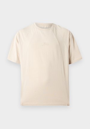 T-shirt beige à manches courtes et col ras du cou, avec des coutures incurvées subtiles et un petit logo embossé au centre de la poitrine.