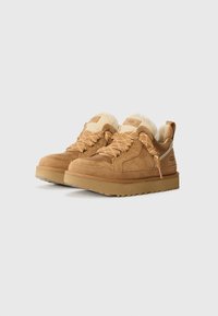 Adidași din suede bej cu o guleră căptușită, accente crem, șireturi texturate și o talpă din cauciuc_chunky. Brandul este vizibil pe limbă și pe toc.