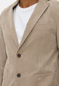 Beige Cordblazer mit Reverskragen, zwei Knöpfen und einer Brusttasche. Der Stoff hat eine strukturierte, gerippte Oberfläche.