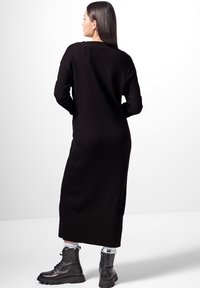 Robe noire longue à côtes avec des épaules tombantes, tissu texturé, et une silhouette droite, associée à des bottes de combat noires à lacets.
