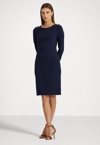 Rochie bleu marin, cu mâneci lungi, cu o siluetă ajustată, accente cu nasturi aurii pe umeri și textură de tricot neted.