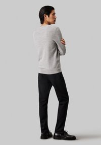 Suéter de punto gris con mangas largas, cuello redondo y dobladillo acanalado, combinado con jeans negros y zapatos negros de cordones. Fondo liso.