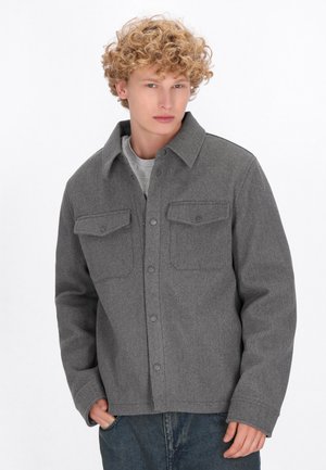 Gray wool-blend jacket featuring a button front, two chest pockets, pointed collar, and long sleeves, paired with blue denim.