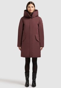 Burgundia värvi polsterdatud mantel kõrge kraega, küljetaskutega ja esiosa tõmblukuga. Omab keskmise pikkusega lõiget ja on valmistatud siledast materjalist.