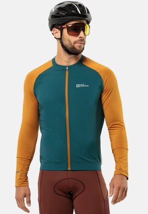 Langärmliges Radtrikot in Petrol und Orange mit durchgehendem Reißverschluss, reflektierenden Akzenten und Logo auf der Brust. Kombiniert mit eng anliegenden braunen Shorts.