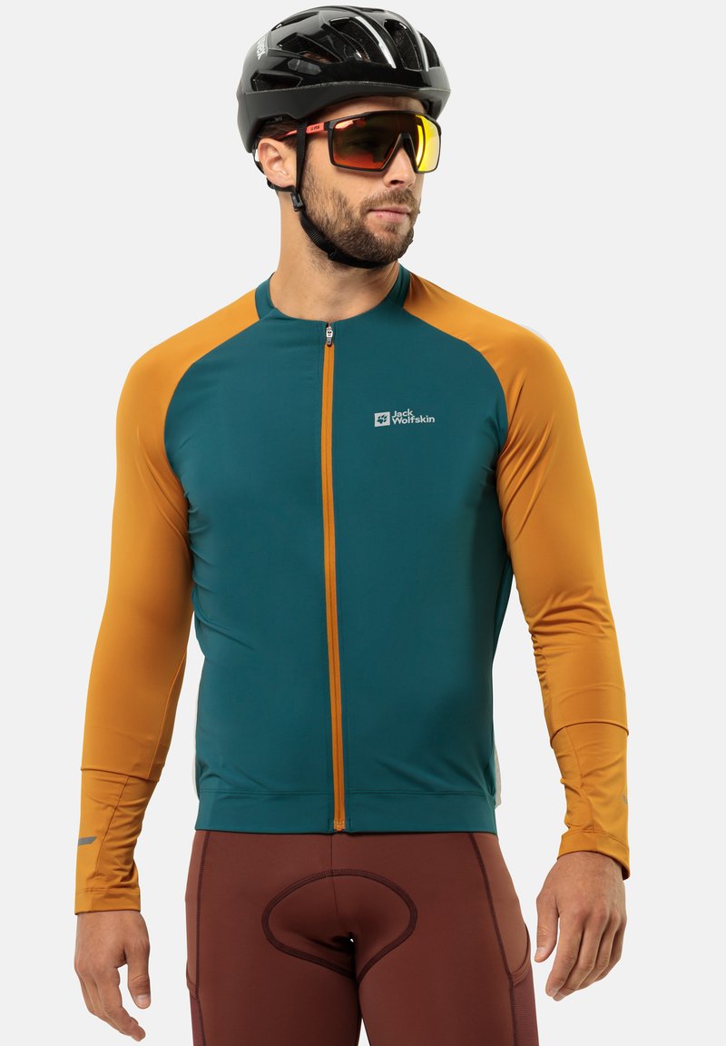 Maillot de cyclisme à manches longues en teal et orange avec une fermeture éclair sur toute la longueur, des accents réfléchissants et un logo sur la poitrine. Associé à un short ajusté marron.