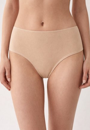 Donna che indossa biancheria intima beige in cotone a vita alta, mostrata dalla vita a metà coscia contro uno sfondo neutro.