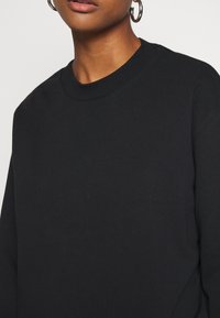 Sweat-shirt en coton noir avec un col rond, une coupe ample et des manches longues. Présente une texture lisse et un design simple sans motifs ni accents.
