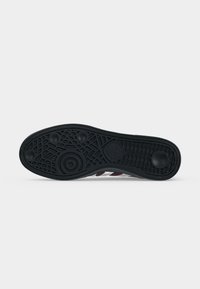 Μαύρη λαστιχένια σόλα παπουτσιού Adidas με υφή και κυκλικά λαβές, εμφανίζεται από κάτω σε απλό φόντο.