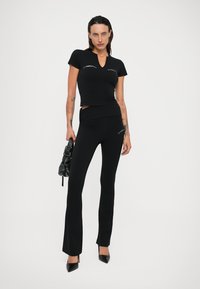 Zwarte cropped t-shirt en aansluitende flared broek van rekbare stof, met witte merklong. Accessoires omvatten een zwarte textured tas.