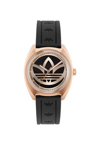 Montre avec bracelet en caoutchouc noir, boîtier en or rose, cadran noir avec un grand design de logo et aiguilles métalliques. Accents de bracelet texturé inclus.