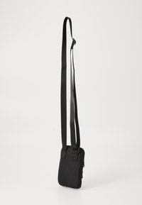 Melna crossbody soma, kas izgatavota no izturīga auduma. Aprīkota ar regulējamiem siksnām, rāvējslēdzēja aizdari un divām akcentējošām siksnām priekšpusē.