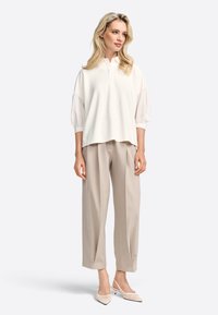 Hvid skjorte med ballonærmer, kombineret med lyse beige brede bukser og cremefarvede spidse slingback hæle. Glatte teksturer.