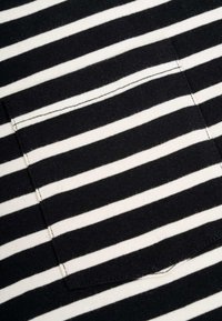 Schwarz-weißer gestreifter Stoff mit strukturierter Oberfläche, der eine auf die Streifen ausgerichtete aufgesetzte Tasche und präzise Nähdetails aufweist.