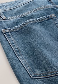 Detailní záběr modré džínové látky zobrazující zadní kapsu a švy na páru džín.