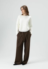 Witte gebreide trui met een ronde hals en lange mouwen, gecombineerd met losse, hoge taillerijke broek in bruin met een strikdetail.