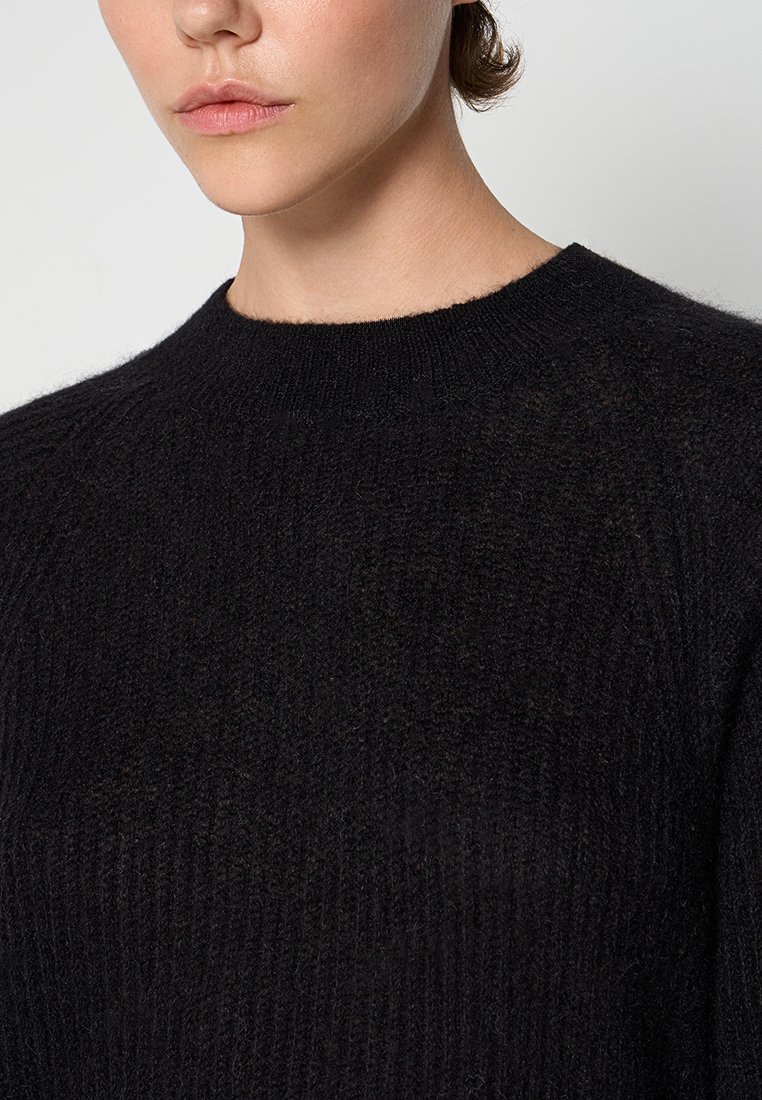 Schwarzer Strickpullover mit rundem Halsausschnitt und gerippter Textur. Der Stoff ist weich mit einem leichten Schimmer und minimal sichtbaren Nähten.